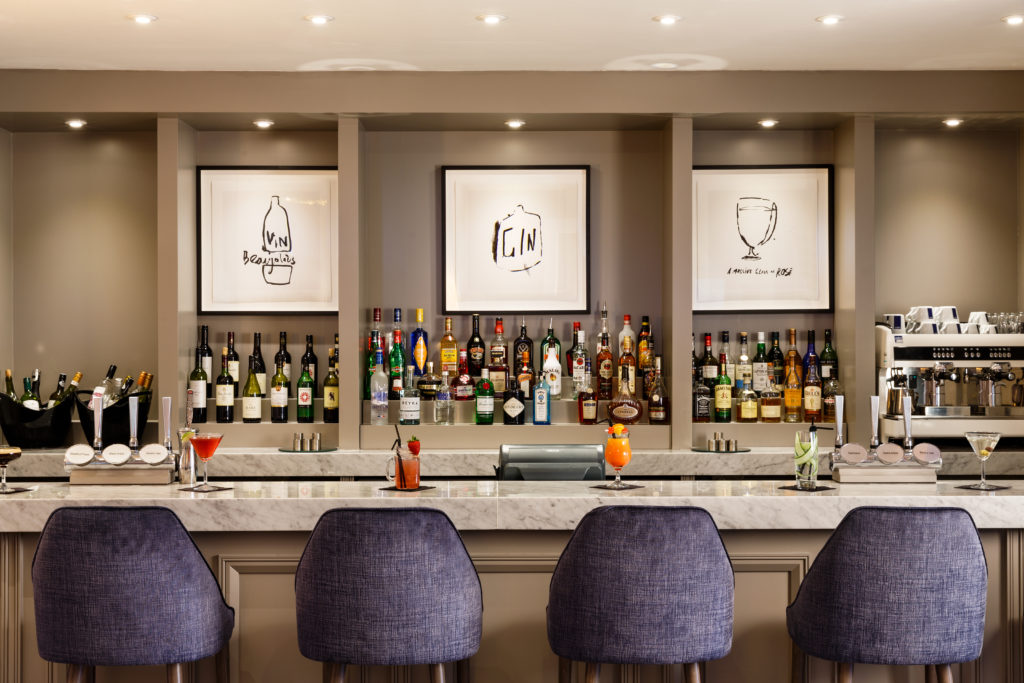 The bar at Mercure Gloucester Bowden Hall Hotel with bottles of spirits lined up on shelves and cocktails on the counter
