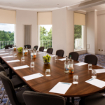 Long table seating 18 in The Congress Room at mercure gloucester bowden hall hotel ready for a meeting, with notepads, bottles of water and bowls of apples on the table