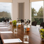 Close up of long table seating 18 in The Congress Room at mercure gloucester bowden hall hotel ready for a meeting, with notepads, bottles of water and bowls of apples on the table