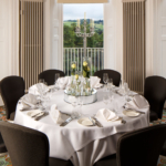 Round table with place settings for lunch in front of an impressive bay window in the Presidential Room at mercure gloucester bowden hall hotel