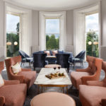 Long shot of the lounge area with assorted sofas and chairs in front of a large window and sandwiches on a table in the foreground at mercure gloucester bowden hall hotel